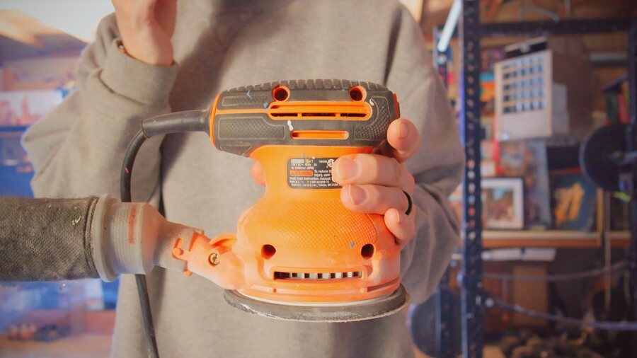 Jake DeBus holding an orbital sander in the studio